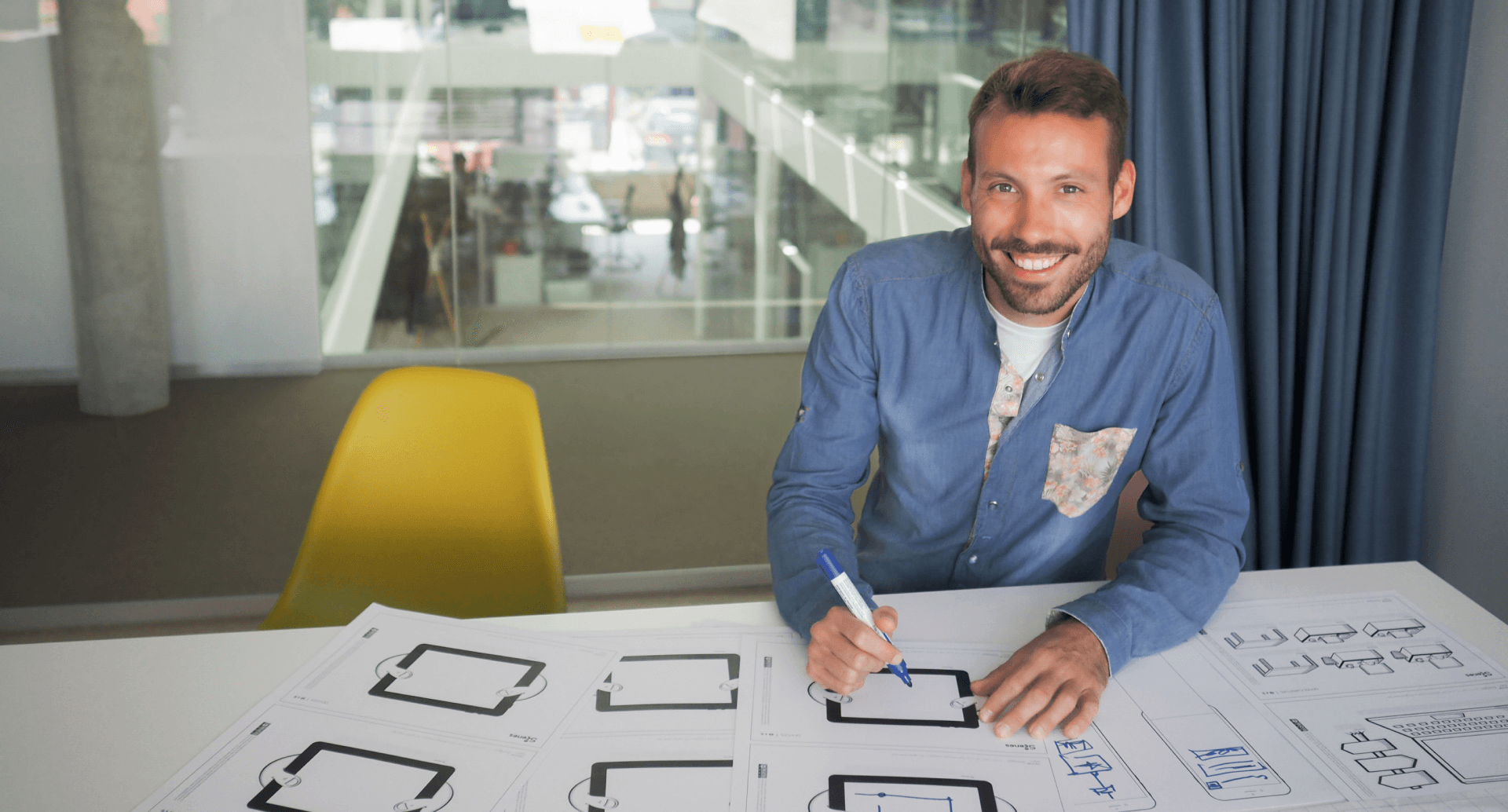 Ein Mann strahlt in die Kamera. Er hält einen Stift und zeichnet Prototypen