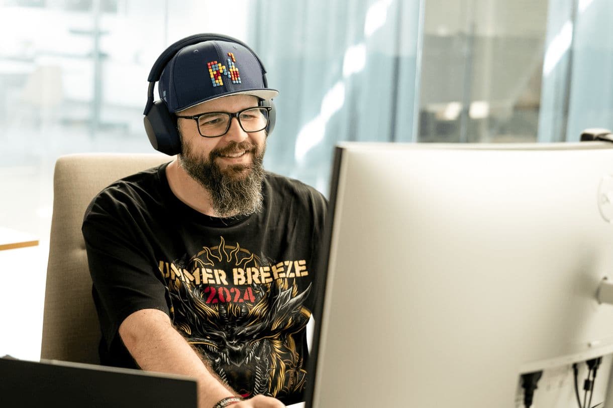Mitarbeiter mit Cappy und Headset lächelt in seinen Bildschirm. Er trägt ein Summer Breeze 2024 Shirt