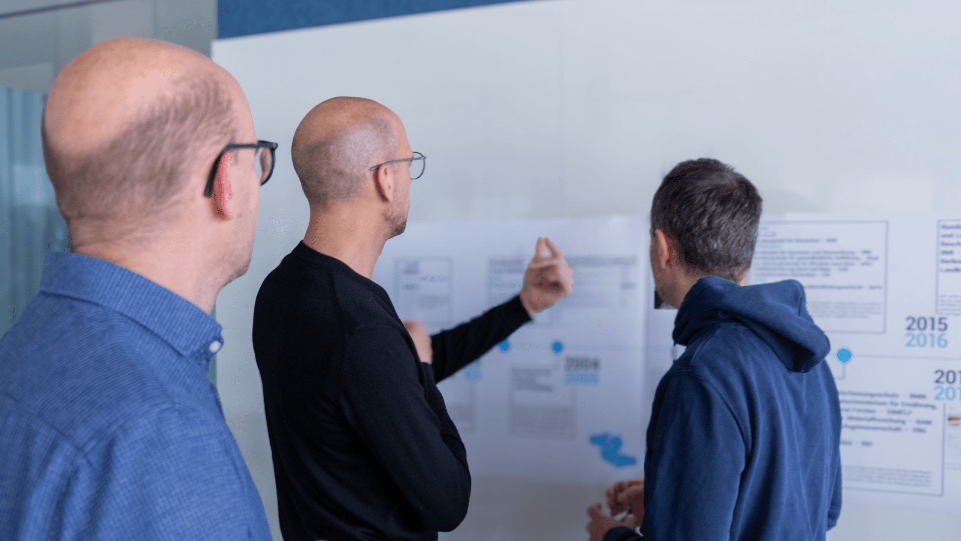 Zwei Männer stehen vor einem Whiteboard. Einer der beiden macht eine erklärende Geste