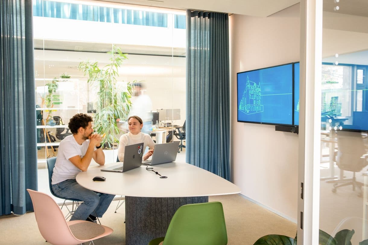 Zwei Mitarbeitende im Besprechungsraum vor ihren Laptops